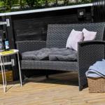 Terrasse mit Gartenbank, Tisch, Flasche und Kissen.
