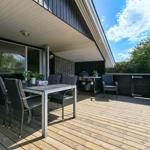 Terrasse mit Tisch, Stühlen und Grill unter Dach. Holzdecke, Sicht auf Bäume.