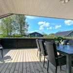 Terrasse mit Tisch und Stühlen, Blick auf grüne Landschaft und Häuser.