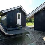 Schwarze Holzhütte mit Terrasse, Liegestuhl und weißem Stuhl.