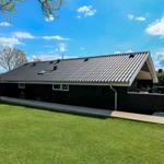 Schwarzes Haus mit Holzterrasse und grünem Rasen unter blauem Himmel.