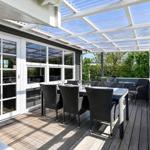 Terrasse mit Tisch, Stühlen und Dachkonstruktion. Durchgehendes Glasfenster zur Inneneinrichtung.