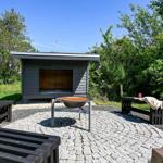 Außenbereich mit Sauna, Grill und Bänken auf Steinplatten.