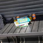 Tisch mit Spielen, Getränken und Fellkissen unter einer Holzveranda.