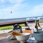 Tisch mit Gläsern und Schalen auf Terrasse mit Blick auf Wasser und Kitesurfer.