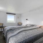 Schlafzimmer mit Bett, zwei Stühlen und Fensterblick auf Wasser.