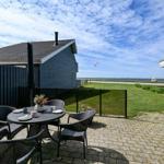 Terrasse mit Tisch und Stühlen, Blick auf Grasfläche und Strand.