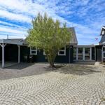 Haus mit Kiesweg, Carport und Baum unter blauem Himmel.