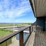 Terrasse mit Tisch und Stühlen, Blick auf Grünfläche und Wasser.