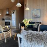 Wohnbereich mit Sofa, Stuhl und Küchenzeile. Holzwände und Beleuchtung.