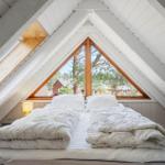 Schlafzimmer mit Dachschrägen, großem Fenster und Bett mit weißen Decken.