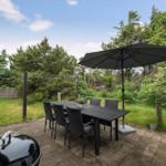 Terrasse mit Tisch, sechs Stühlen und Sonnenschirm. Grill und Pflanzen sind vorhanden.