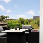 Terrasse mit Sitzgruppe und Tisch. Blick auf Grünfläche und Himmel.