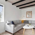 Wohnzimmer mit grauem Sofa, weißem Tisch und Fensterblick auf Garten.