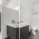 Badezimmer mit Waschbecken, Toilette und Dusche. Weiße Wände, graue Fliesen und moderne Einrichtung.
