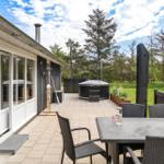 Terrasse mit Sitzgruppe, Whirlpool und Garten. Holzhaus mit Glastüren und Dach.