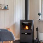 Kaminofen mit brennendem Feuer, graue Sitzgelegenheit, Fenster mit Blick auf Grün