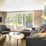Wohnzimmer mit Sofa, Sessel und TV. Durchgang zum Balkon mit Blick auf Grün.