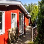 Rotes Holzhaus mit Terrasse und Fenstern. Holztor und Bäume sind sichtbar.