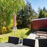 Terrasse mit Tisch, Stühlen und Sonnenliegen neben rotem Haus. Grünfläche und Bäume im Hintergrund.