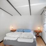 Schlafzimmer mit Bett, zwei Nachttischen und Fenster mit Vorhängen.