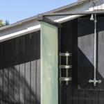 Außen-Dusche mit Duschbrause und Halter an schwarzer Holzwand.