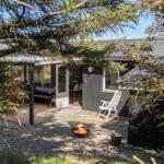 Hütte mit Terrasse, Sitzgelegenheit und brennendem Feuerkorb unter Bäumen.
