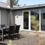 Terrace with table and chairs in front of a house with glass doors.