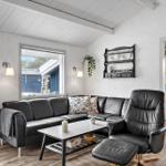 Wohnzimmer mit Sofa, Sessel und Tisch. Küche im Hintergrund. Weiße Wände und Holzboden.