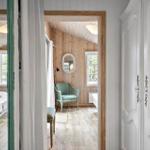 Schlafzimmer mit Holzwand, Bett und Stuhl. Blick in einen Flur mit Spiegel und Fenster.