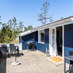 Blauer Ferienhaus mit Terrasse, Grill und Sitzgelegenheiten. Umgeben von Bäumen und klarem Himmel.