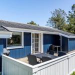 Ein blaues Ferienhaus mit Terrasse, Tisch und Stühlen. Hinterhof mit weißem Zaun und Bäumen.
