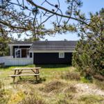 Ein dunkel gestrichenes Ferienhaus mit weißem Balkon und Picknicktisch im Gras.