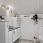 Badezimmer mit Waschbecken, Spiegel, Toilette und Pflanze an der Wand.