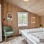 Schlafzimmer mit Holzwand, Bett, Sessel und Fenster