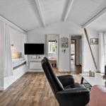 Wohnraum mit Holzboden, Sofa, Fernseher und Blick in Schlafzimmer.