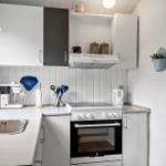 Küche mit Spüle, Herd und Kühlschrank. Weiße Schränke und Holzwand.