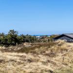 Schwarzes Haus auf Dünen mit Blick auf das Meer unter blauem Himmel.