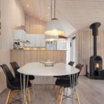 Essbereich mit Tisch, Stühlen und Kaminofen. Küche mit weißen Schränken. Holzwände und Decke.