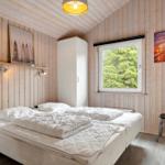 Schlafzimmer mit Holzwand, Bett, Fenster und Stuhl.