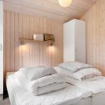 Schlafzimmer mit weißem Bett, Holzwänden und weißen Schränken. An der Wand hängt ein kleiner Holzregal mit Bildern.