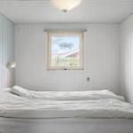 Schlafzimmer mit weißem Bett und Fenster. Wände sind weiß verkleidet.
