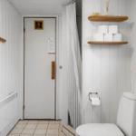 Badezimmer mit Toilette, Dusche und Holzregalen mit Toilettenpapier.