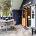 Deck with table and chairs in front of a house with wooden door and window.