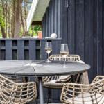 Round table with chairs and wine glasses on a terrace in front of a dark wooden house.