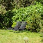 Two black lounge chairs are on a green lawn between shrubs and trees.