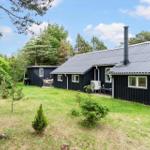 Black cabin with garden and barbecue area. Wooden siding and metal roof.