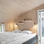 Bedroom with wooden walls and ceiling, white bed, and sliding door to balcony.
