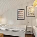 Room with two beds, white walls, and wooden ceiling. Two framed pictures hang on the walls.