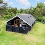 Black wooden house with balcony, surrounded by lawn and trees.